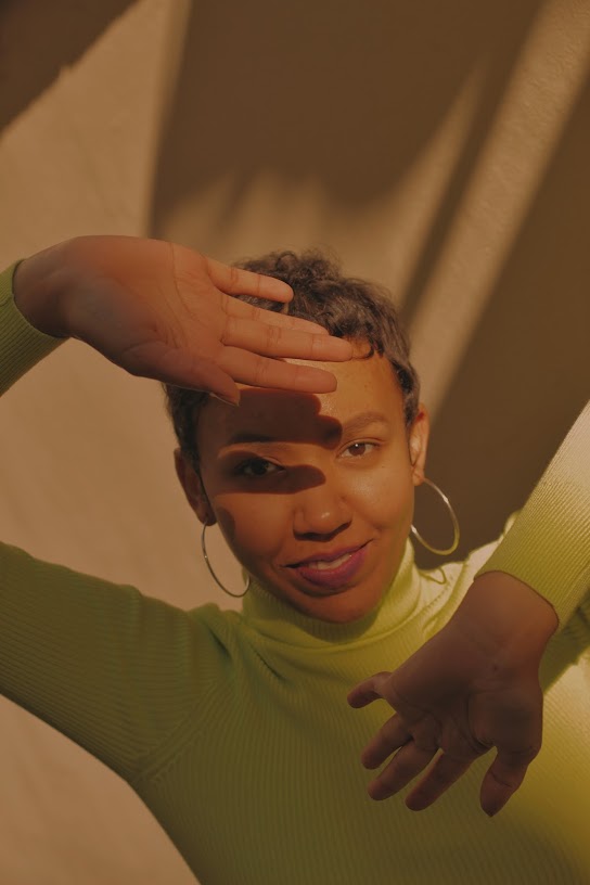 Kanini in a green turtleneck reaching toward the camera